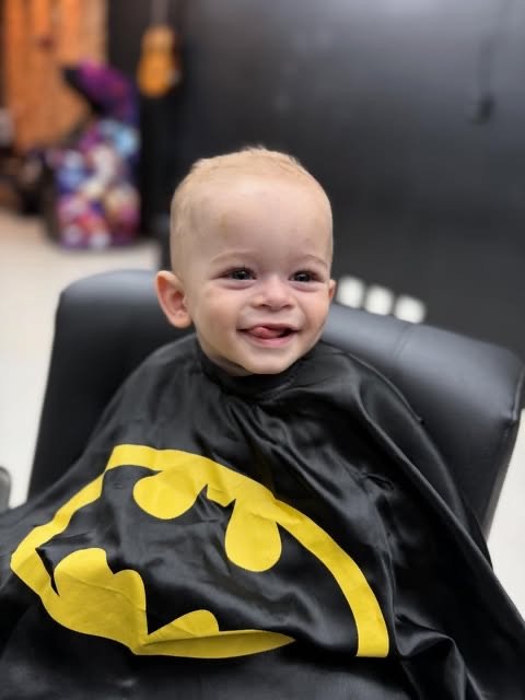 Bebê sorridente com capa do Batman após o primeiro corte